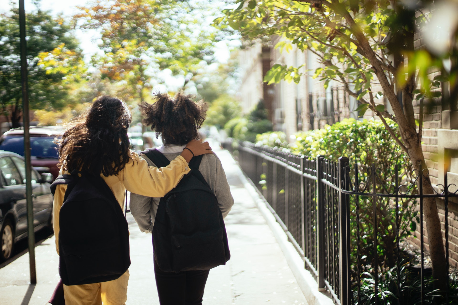 Two students walking to school with backpacks, one has a hand over the other students shoulder.