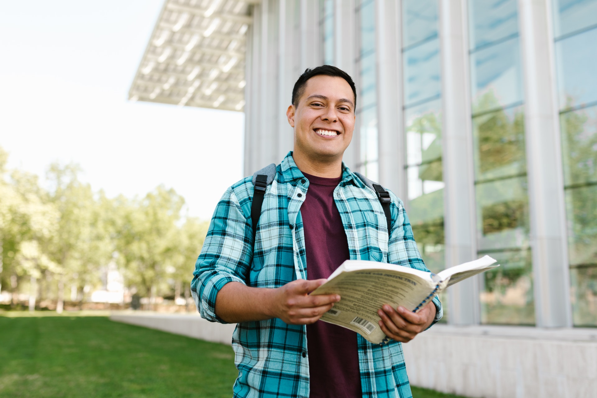 Male teacher holding book, standing outdoors and smiling